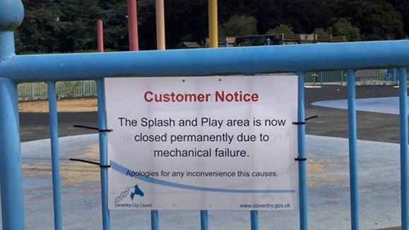 A sign on a blue fence stating the 'splash and play area is now permanently closed'
