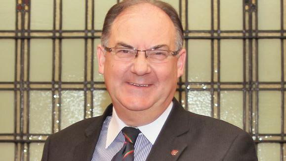 Geoffrey Corkish smiling. He is wearing glasses and a dark suit with a stripy tie.
