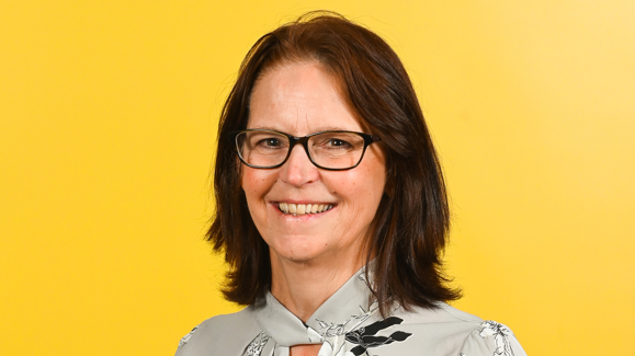 A head and shoulders image of Prof Paula Kersten against a yellow backdrop. She is wearing glasses and smiling and looking into the camera.