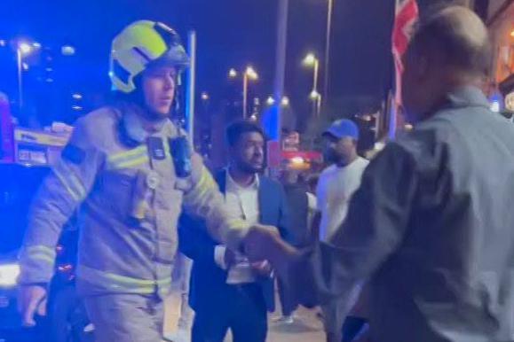 The scene outside the restaurant during the fire with a firefighter walking among others who are standing on the pavement