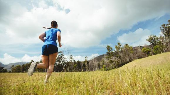 A young woman in blue t-shirt and black shorts running across grass 