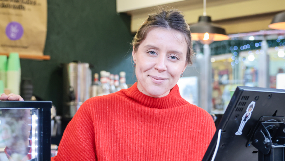 Marta Biegaj, wearing a red jumper, smiles as she works behind the till on her stall