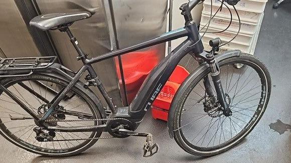 A black e-bike leaning against a metal cabinet