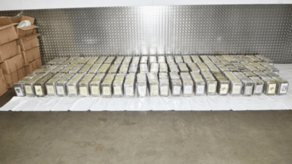 Dozens of white blocks of cocaine lined up in rows on a white sheet. There are markings on the end of each one on a white sticker.