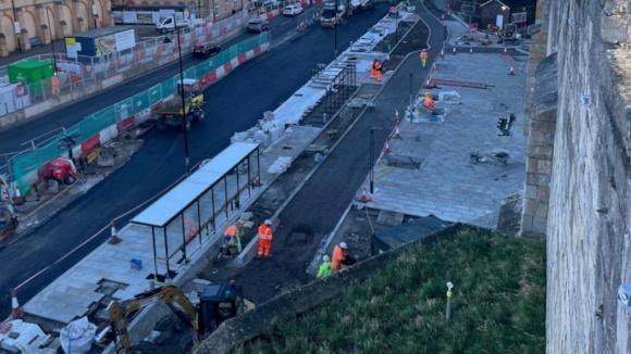 A photo from above shows the area to the front of York Railway Station where new paving has been laid alongside a new bike path. The area is surrounded by scaffolding and people in high vis clothes are working. 