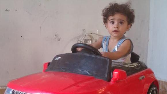 A young child sits in a large, red toy car