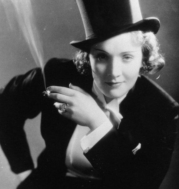 Marlene Dietrich looking to camera while dressed in a top hat and suit, smoking a cigarette