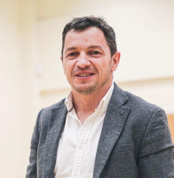 Geraint Evans in white shirt and grey blazer, smiling at the camera.