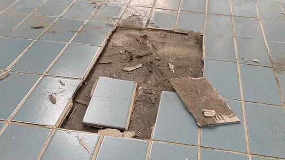 An area of damaged swimming floor tiles. Several of the blue tiles have been removed to show water damage underneath.