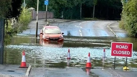 A red car stopped in floods under a bridge