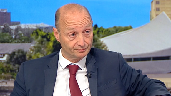 Paul Waugh, wearing a claret tie and navy blue suit sits in the BBC Breakfast studio