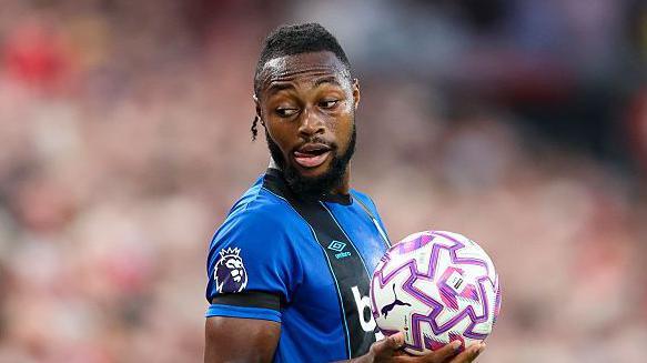 Antoine Semenyo holds a ball as he plans to make a throw-in. He looks over his right shoulder and is wearing the blue and black striped Bournemouth shirt.