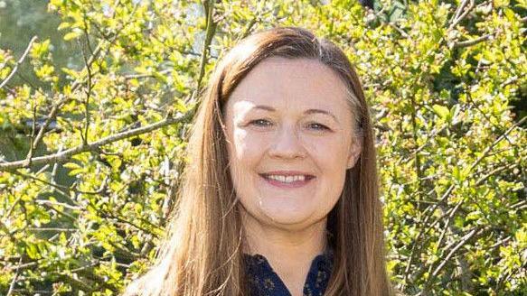 A woman standing in front of tree leaves - she is smiling