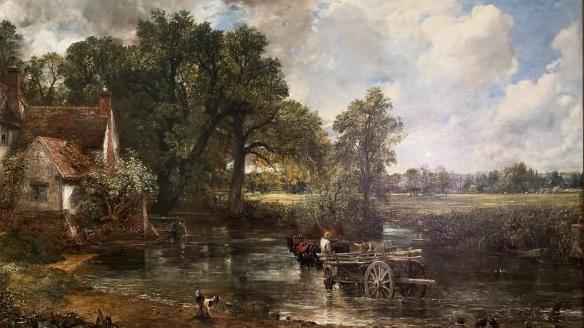 An image of John Constable's Hay Wain oil painting. It depicts a rural scene and features horses pulling a wood wain, or large farm waggon, across a millpond. There is a house to the left, large trees, a field and greenery.