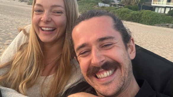 Selfie taken by Jack and Bronwyn. They are smiling and are sat on a beach