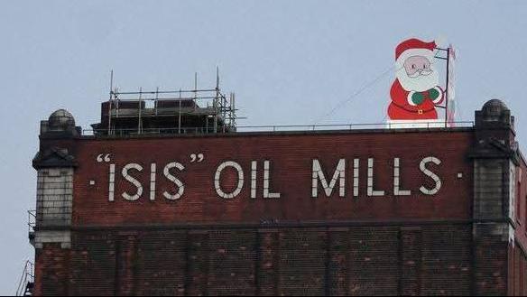 Light-up cartoon Santa figure can be seen on top of a brick silo. The words "Isis" Oil Mills is written in white capitals on the front of the building. 