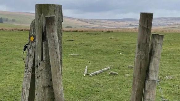 Two wooden posts forming a gateway looking onto moorland and rolling hills.