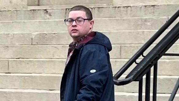 Ieuan Crump wearing a long navy coat and dark glasses, standing in front of steps