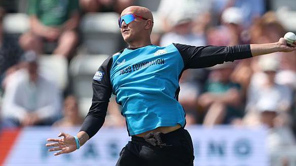 Fateh Singh is about to complete his bowling action in a white-ball game for Worcestershire. He is wearing black trousers and a top with black sleeves and light blue front. He is also wearing sunglasses