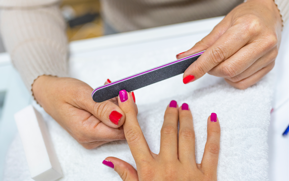 Closeup shot of a woman in a nail salon receiving a manicure by a beautician at nail salon. 