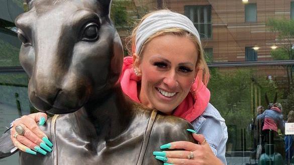 Laura Ellis stood in front of bronze sculpture, wearing Demin jacket and white headband. 