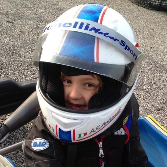 A young Kimi Antonelli sitting in a go-kart while wearing racing overalls and a racing helmet