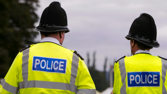 Image shows the backs of two police officers walking away from the camera. They are wearing high-visibility jackers and helmets.