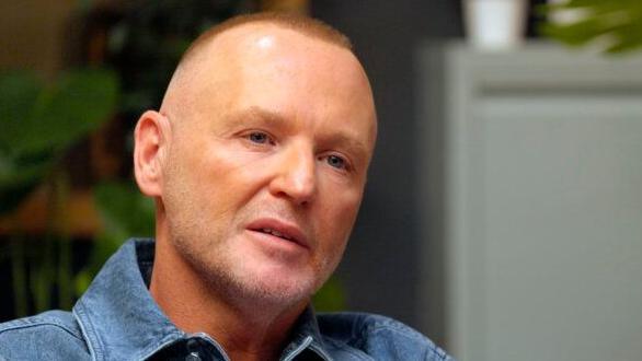 Owen O'Kane, a therapist, wearing blue denim shirt, against blurred interior background