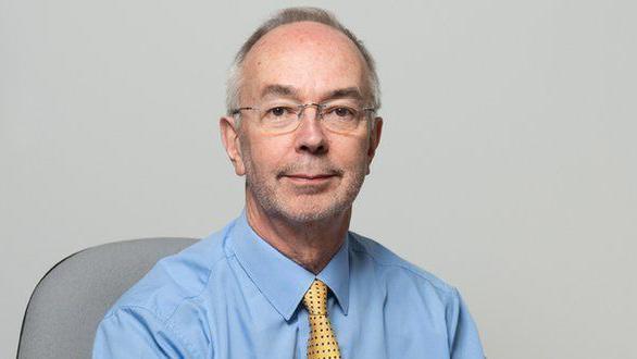 Council leader Martin Tett smiles at the camera. He has short grey hair and is wearing a light blue shirt with a yellow tie that has black spots on it.