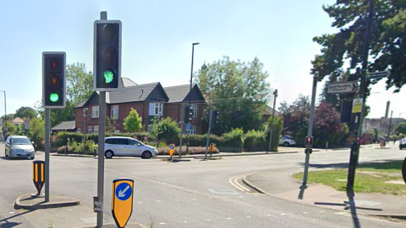 A wide road junction with traffic lights and a pedestrian crossing across Oatlands Drive. Stoke Poges Lane is to the right in the background.