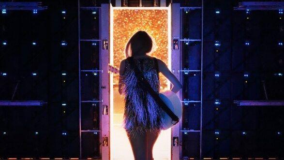 Popstar Taylor Swift walks on to an arena stage holding an acoustic guitar.