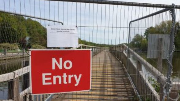 A footbridge boarded up with a red no entry sign attached to the metal railing.