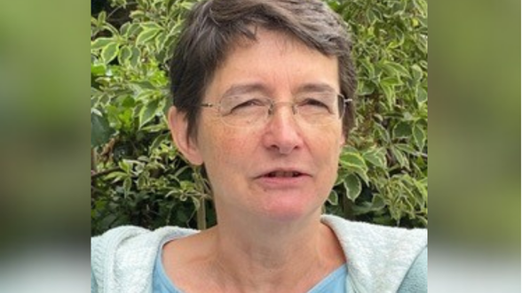 A close-up of Rebecca Nestor standing in front of a hedge. She is wearing glasses.