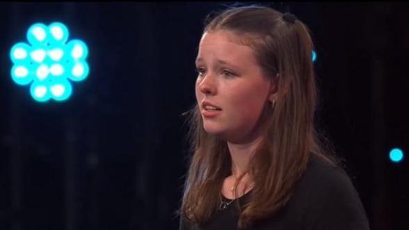 Courtney Manel ar lwyfan yr Eisteddfod yn perfformio. Mae ganddi wallt brown, mae hi'n gwisgo top du, ac mae'r cefndir yn ddu gyda goleuadau glas.