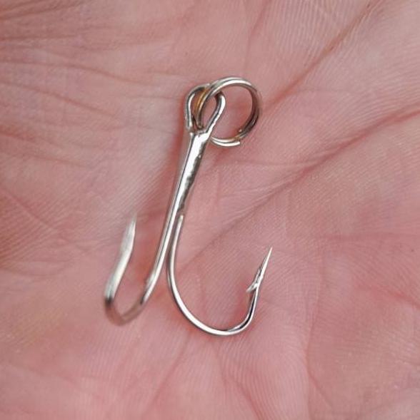 Silver fish hook in the palm of a hand.