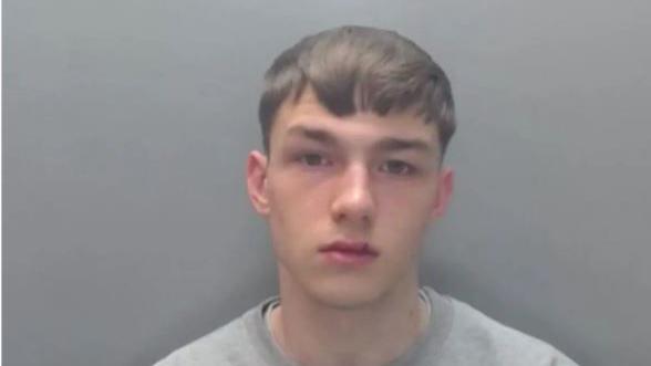 A mugshot of Jack Lawson. He has brown hair and a split upper lip. He is wearing a grey jumper.