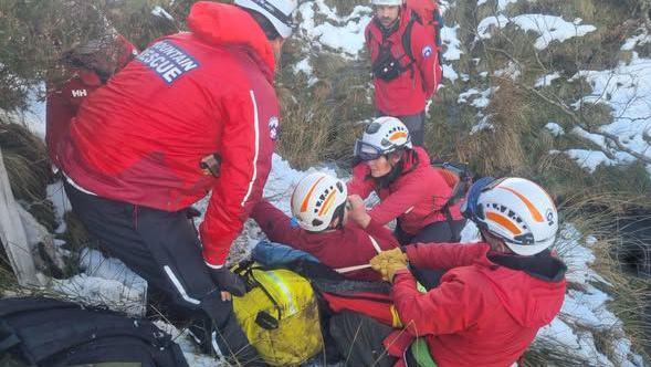 Three mountain rescuers preparing a walker to be winched by helicopter on frozen ground