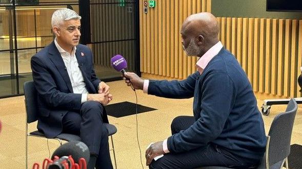 Sadiq Khan sitting on a chair. Opposite is Eddie Nestor, who is holding out a BBC London microphone.