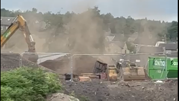 A zoomed in image showing cranes picking up soil on a construction site in the distance