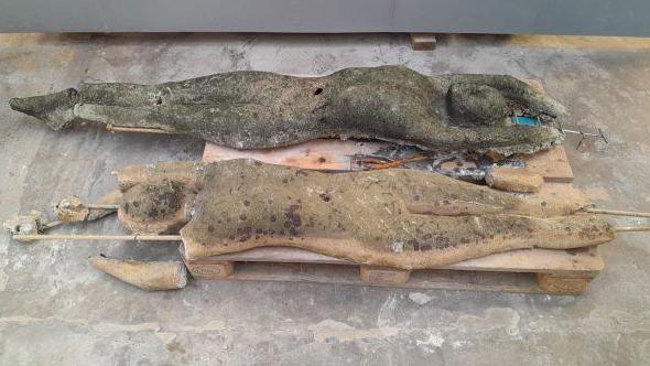 Two eroded cement statues are placed on a pallet on a concrete floor