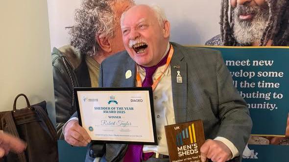 Robert Taylor, wearing a grey suit, smiles broadly as he receives his prize as UK Shedder of the Year at an event in Parliament.