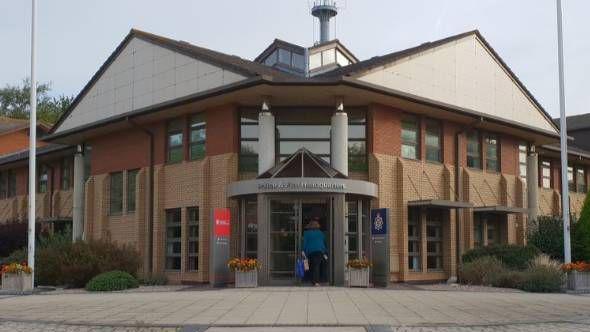 The outside of the fire service headquarters, which is shared with police, in Portishead. It is a large building with a revolving door at the front and two distinctive pointed roofs. Someone can be seen walking into the building, from a distance. 