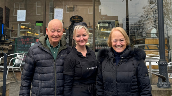 A man and two women smile in front of a shop front.