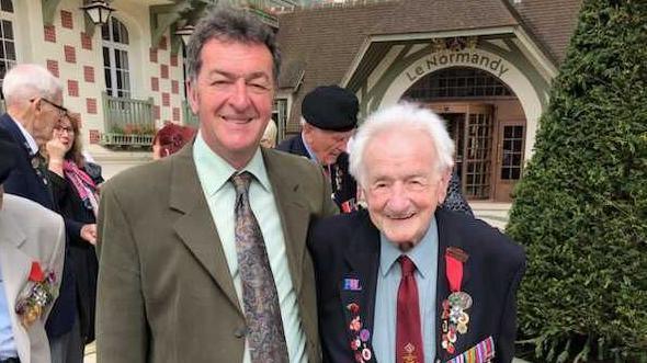 Andrew with his 99-year-old D-Day veteran father, standing infront of a church smiling