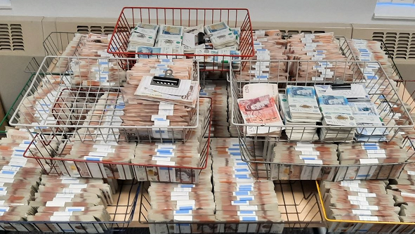 A picture of the cash recovered during the operation, organised on a table in large bundles in a number of different wire baskets. 