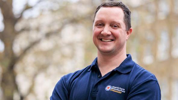 A white man in his late thirties smiles at the camera with his arms folded. He wears an RAF Benevolent Fund Tshirt