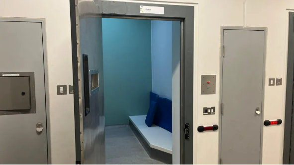 A custody cell with the door ajar, and other doors either side