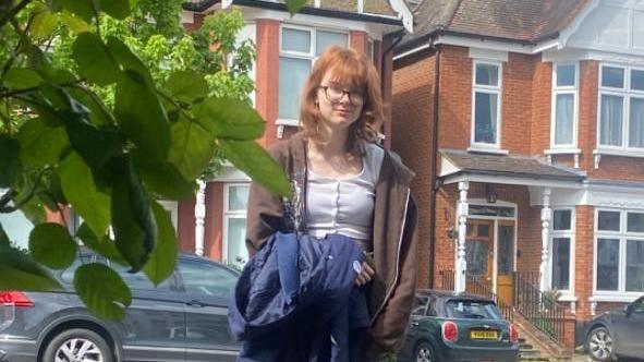 A teenage girl stands outside a house on a residential street