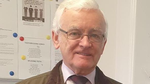 Martin has short platinum-grey coloured hair. He is wearing metal-framed spectacles on his face and is smiling into the camera