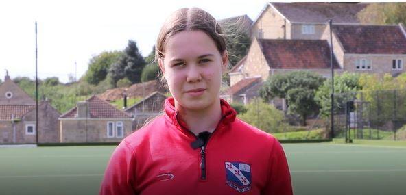 Isabel looking at camera while standing on football pitch with houses behind.